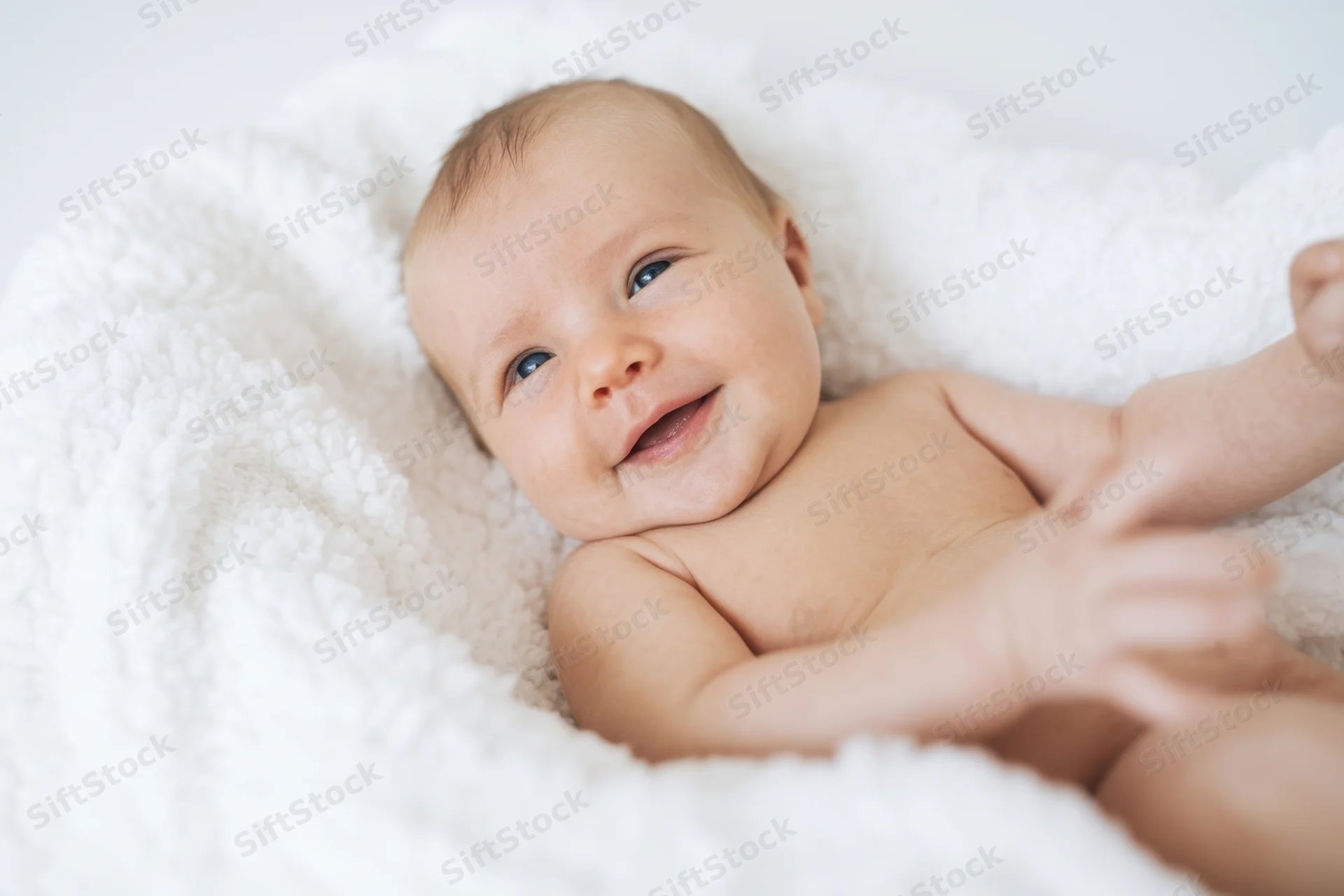 Smiling newborn lying on white plush blanket in soft daylight indoor portrait