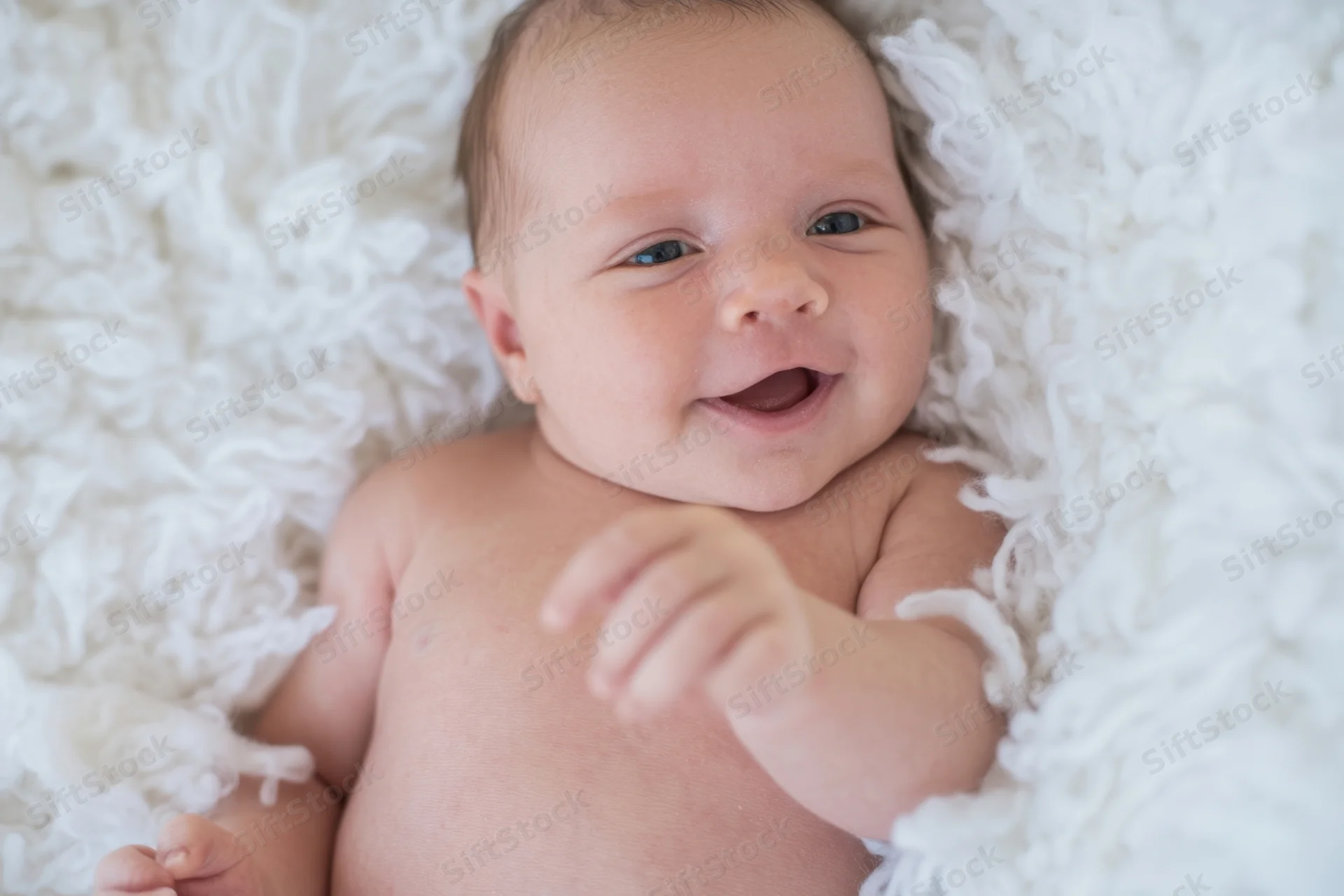Smiling newborn lying on white plush blanket in soft daylight