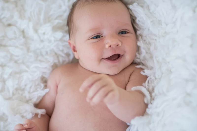 Smiling newborn lying on white plush blanket in soft daylight
