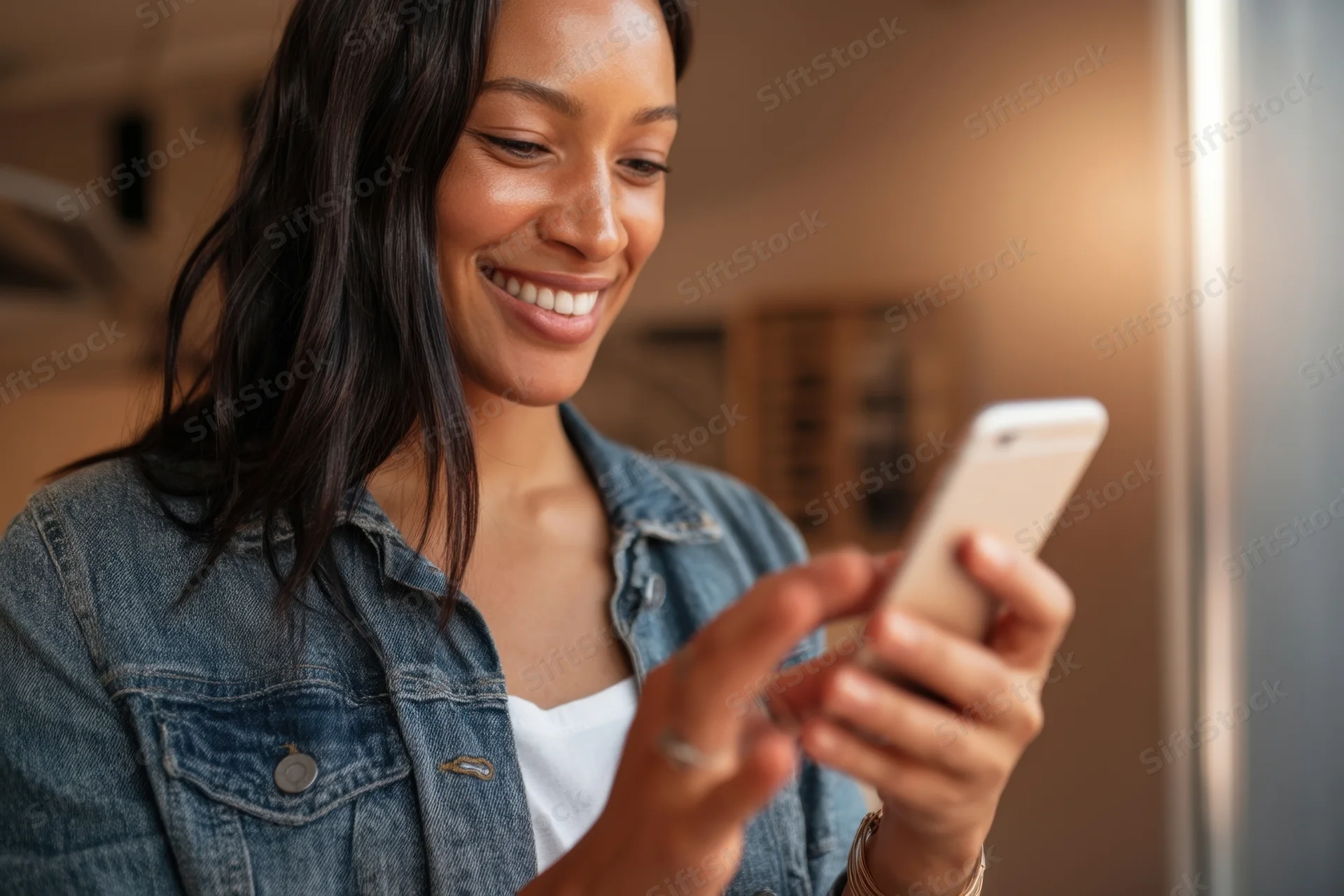Smiling woman holding smartphone in kitchen interior