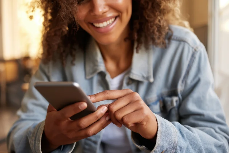 Smiling woman holding smartphone and typing in a warmly lit indoor setting