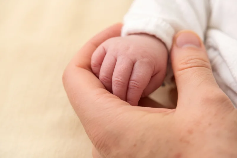 Adult hand gently holding a newborn baby's tiny hand on a soft blanket
