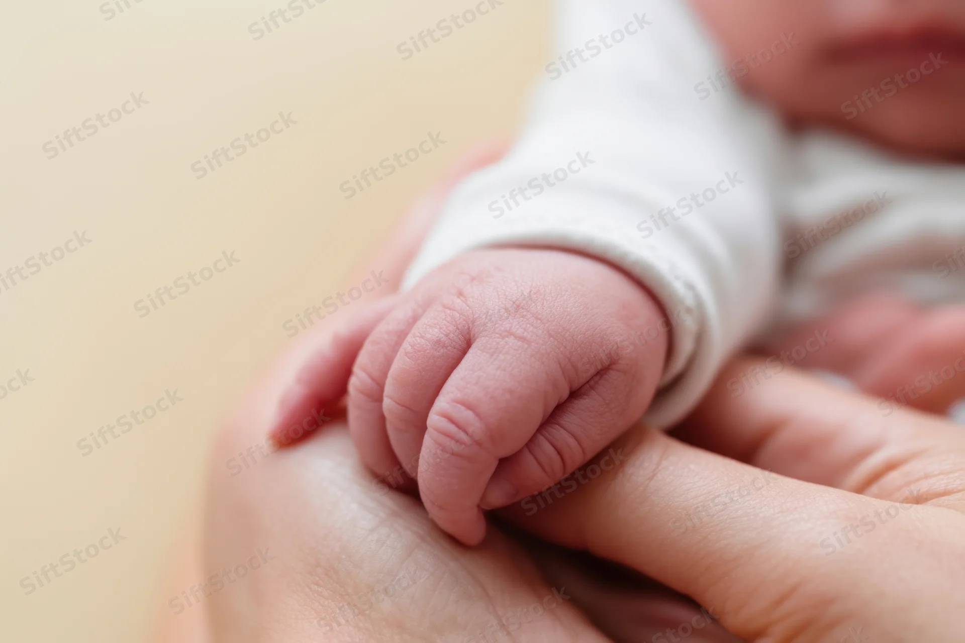 Newborn baby's tiny hand gently held in an adult's palm, close-up view