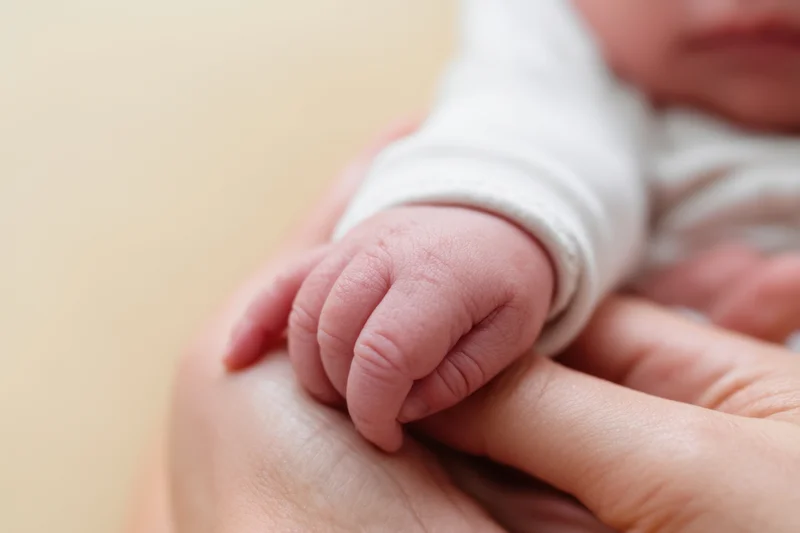 Newborn baby's tiny hand gently held in an adult's palm, close-up view