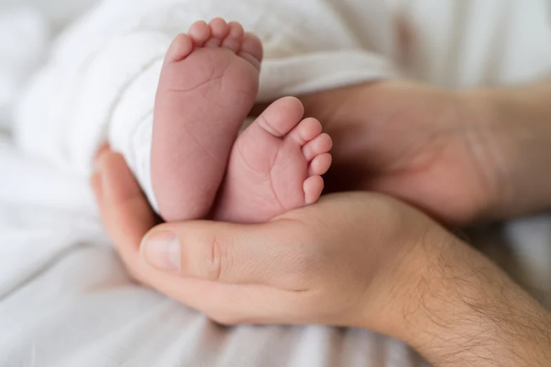 Newborn baby feet cradled in adult hands on soft white blanket