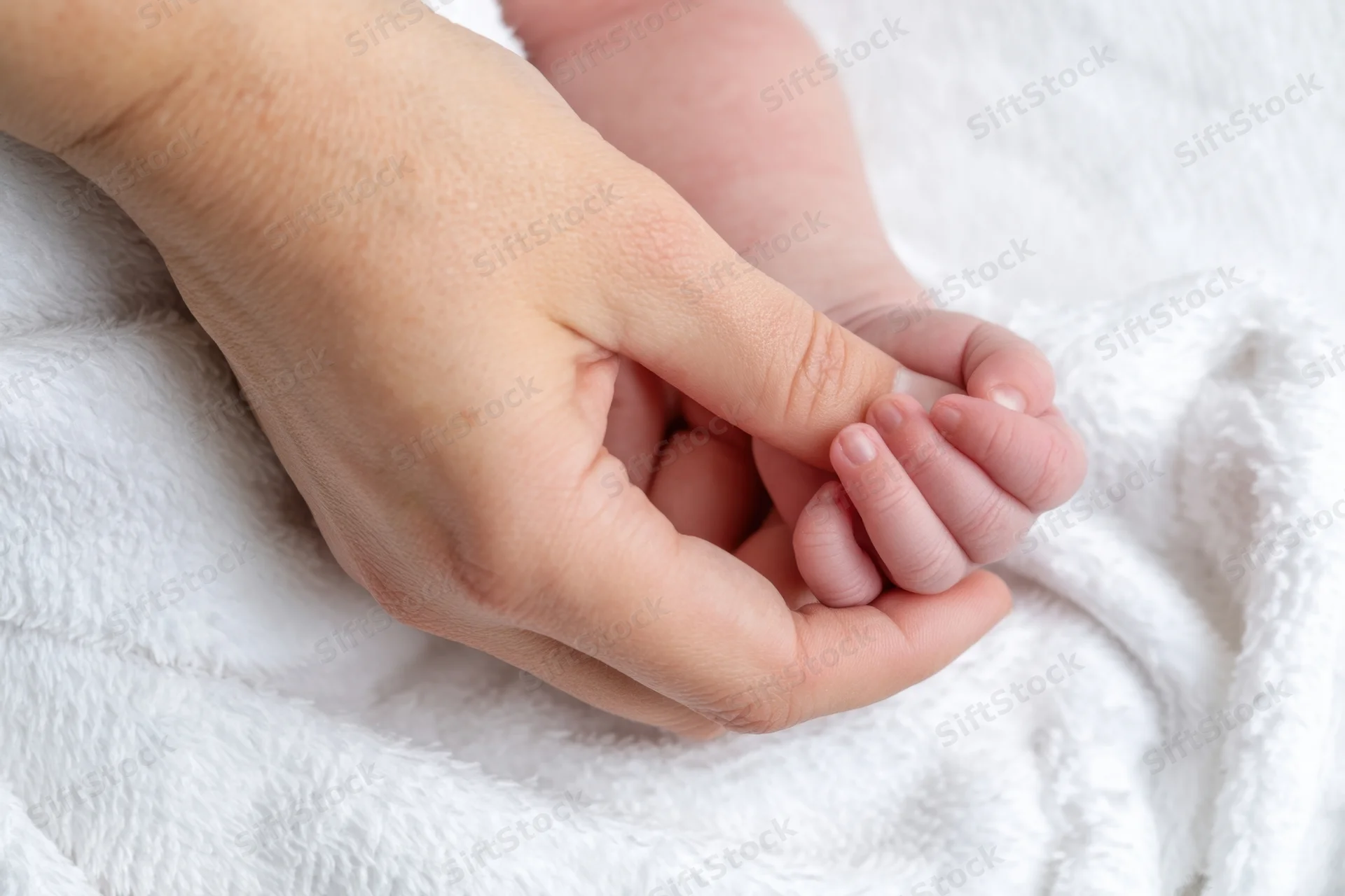 Adult hand gently holding newborn baby's hand on white blanket