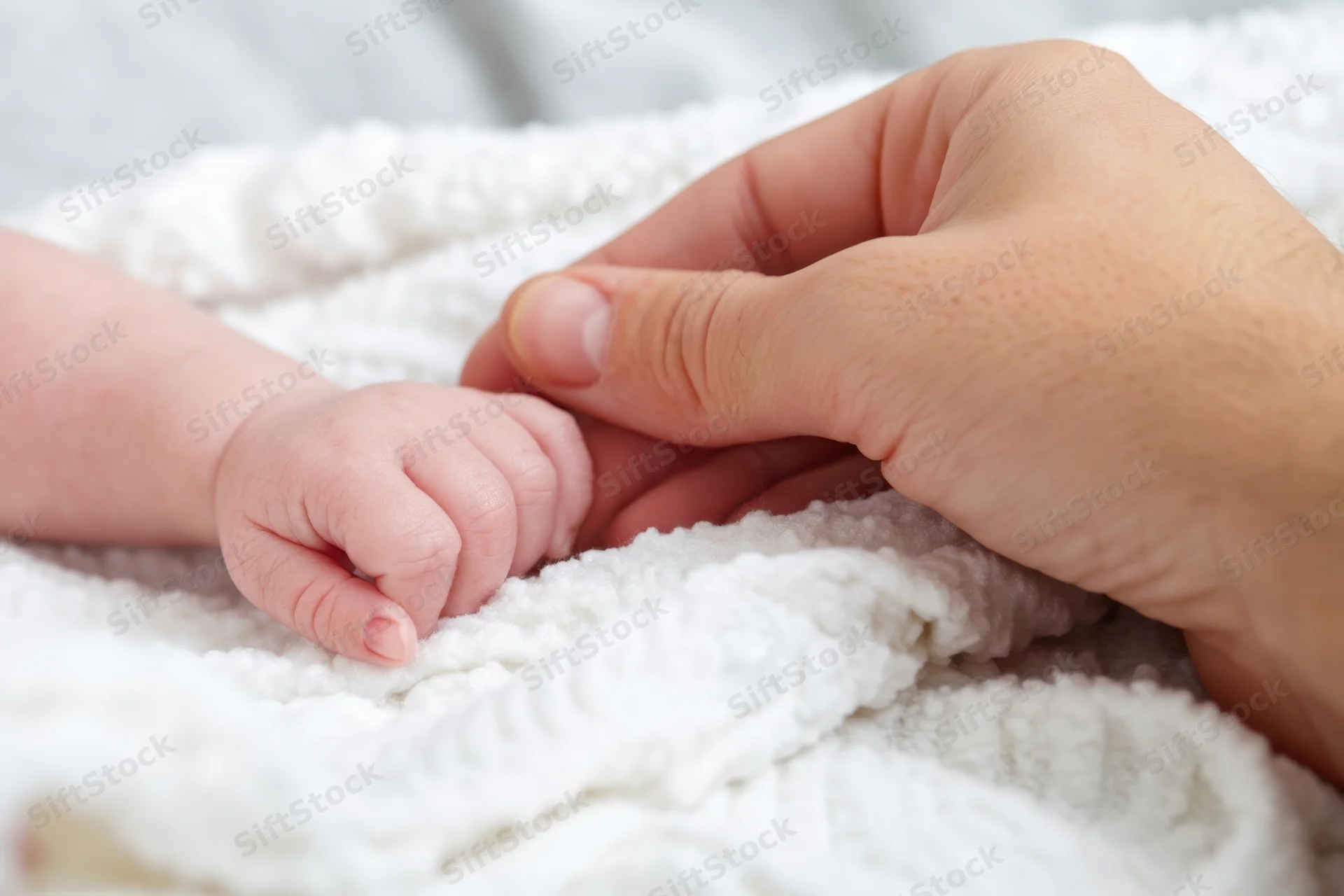 Adult hand gently holding baby's hand on a white knitted blanket