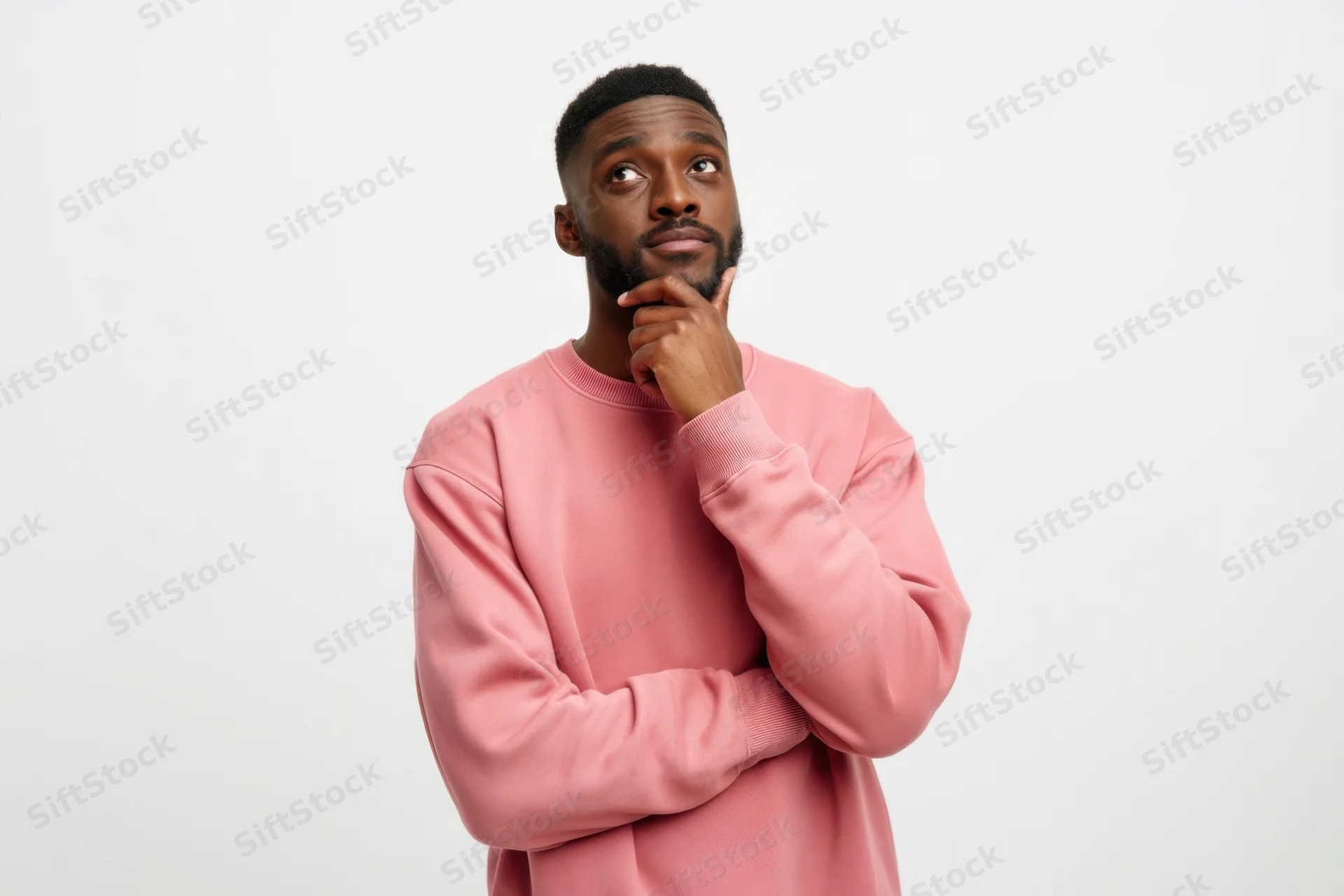 Thoughtful man in pink sweatshirt touching chin while looking up against white background