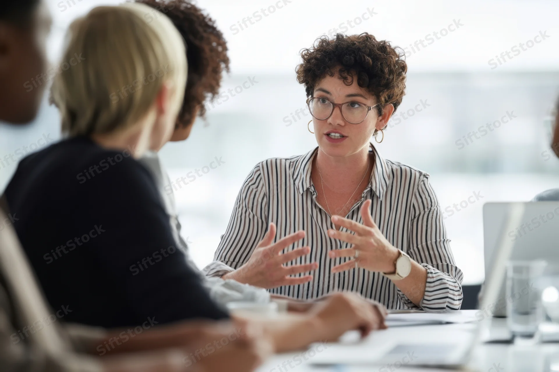 Woman speaking with hand gestures during office meeting with colleagues around table