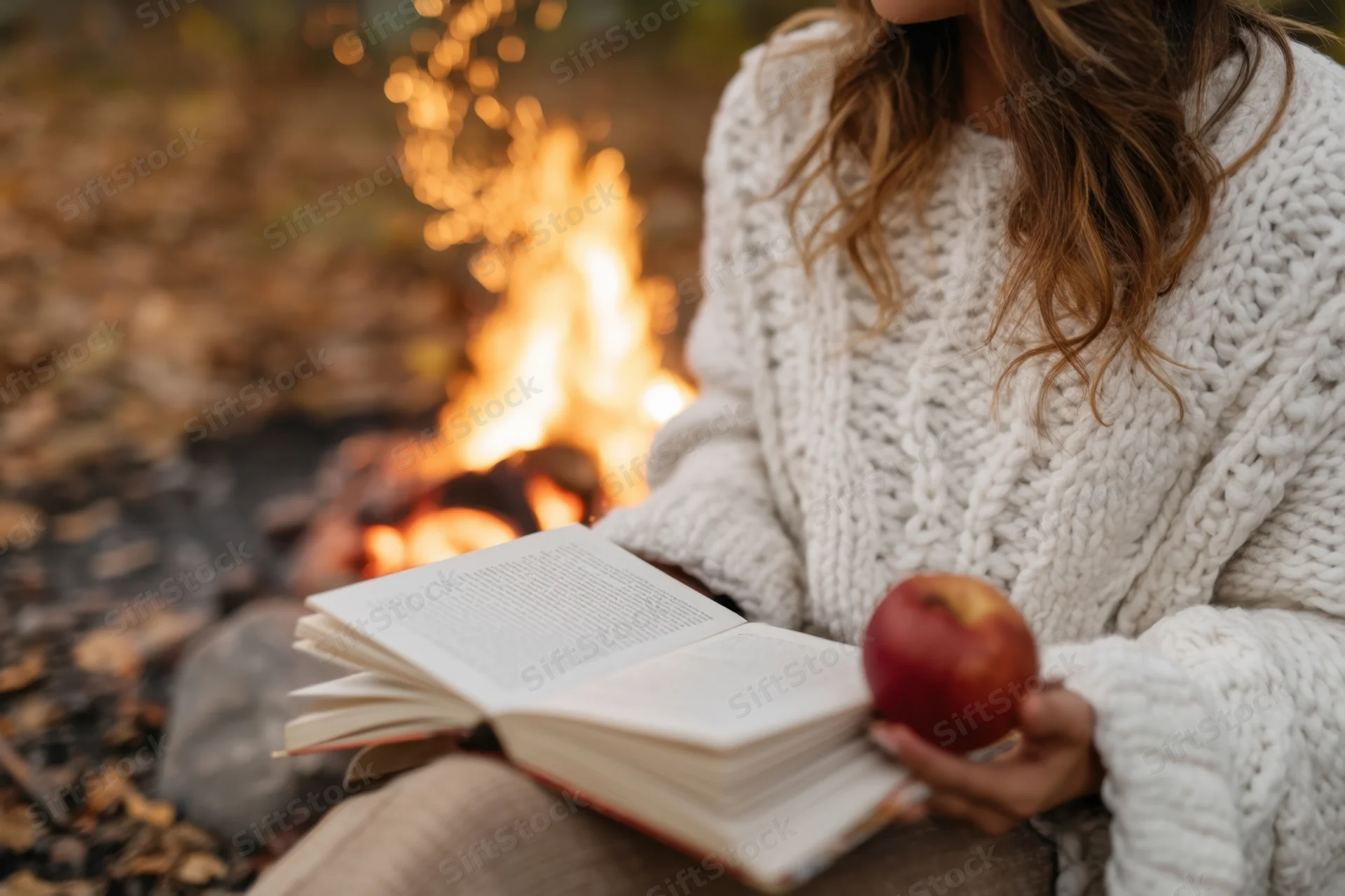 Woman reading a book by a campfire in autumn outdoors