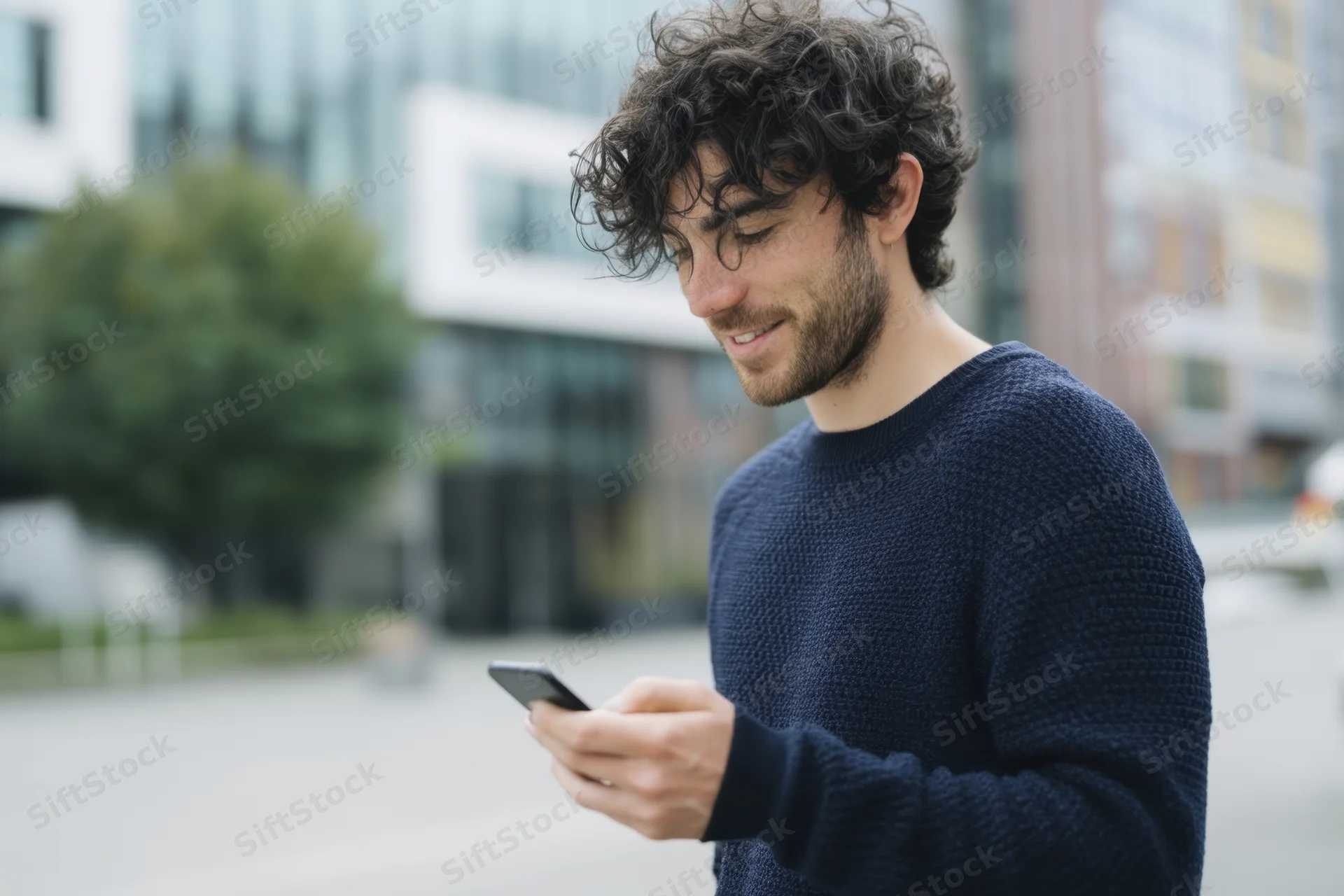 Young man smiling while using smartphone outdoors in city setting