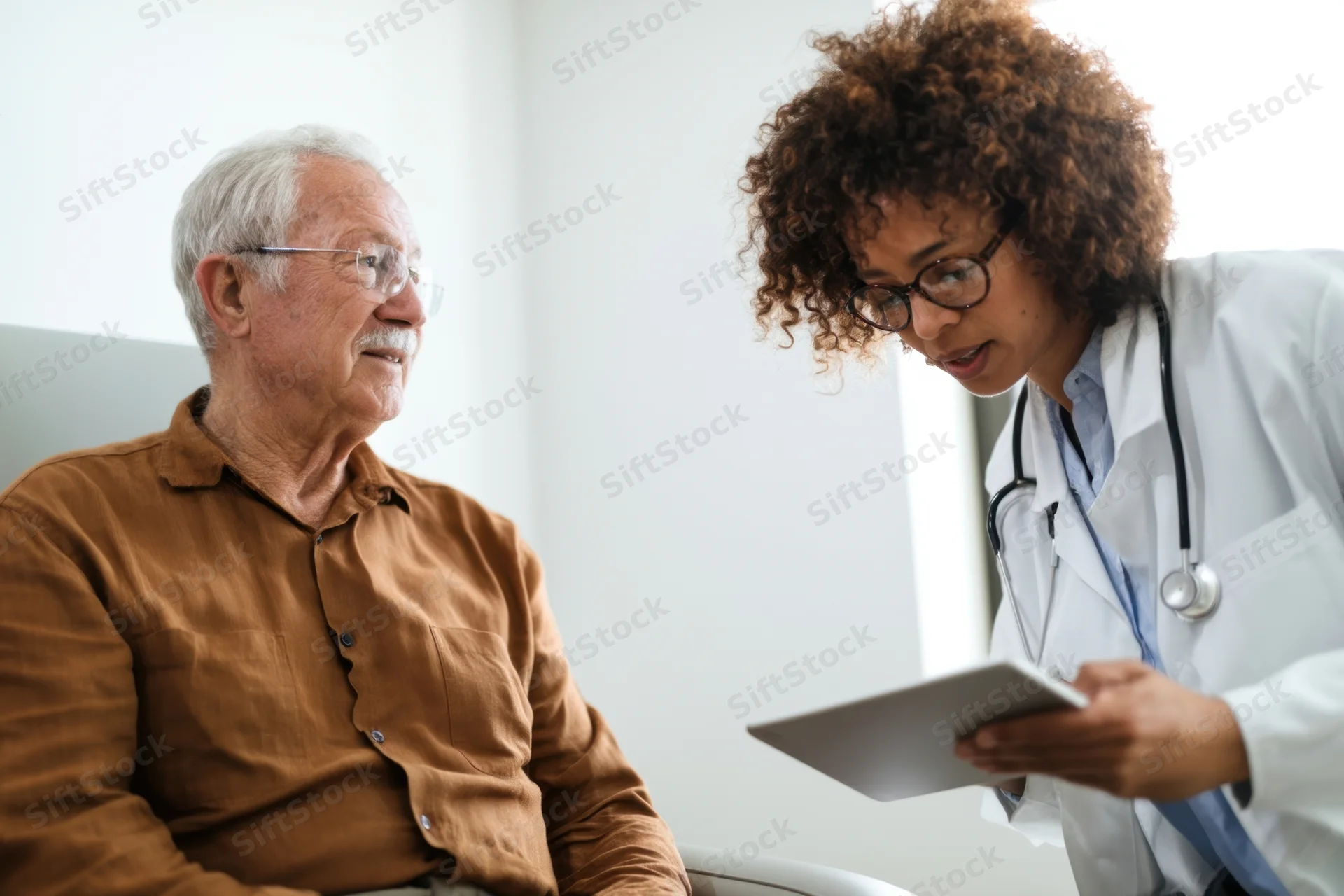 Female doctor discussing medical records with elderly male patient in clinic setting