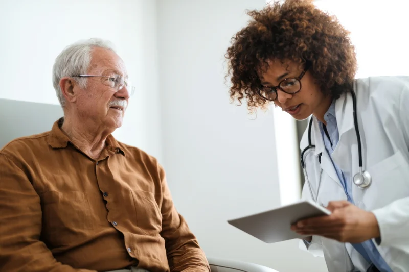 Female doctor discussing medical records with elderly male patient in clinic setting