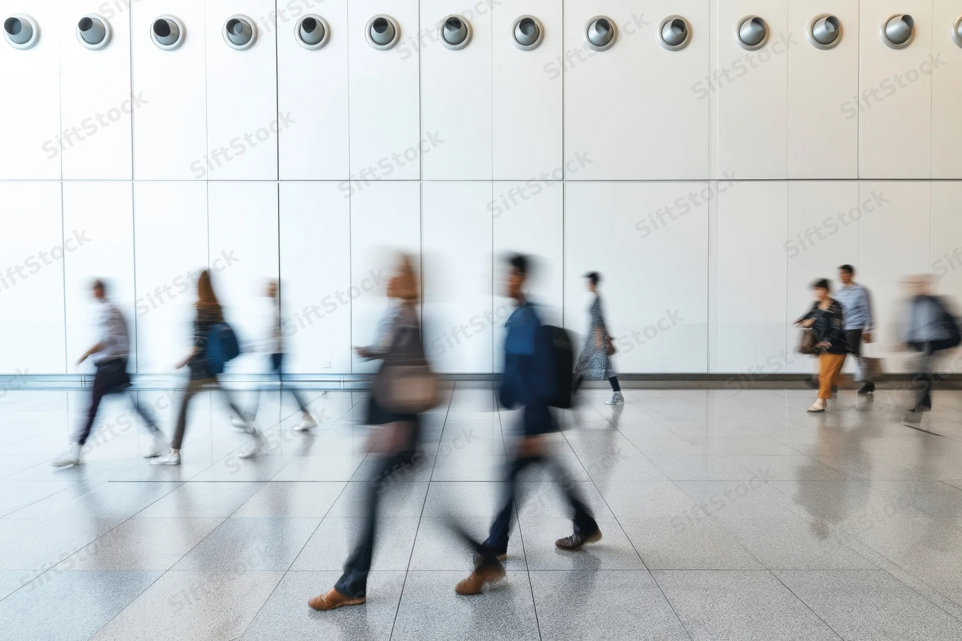 Blurred pedestrians walking through a bright modern atrium with white tiled floor and circular ceiling lights