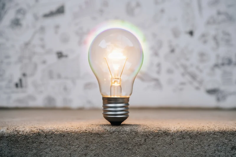 Glowing incandescent lightbulb on textured concrete surface with sketched diagrams in background