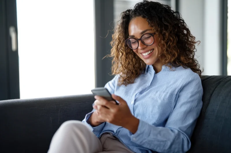 Young woman smiling while using smartphone on couch at home