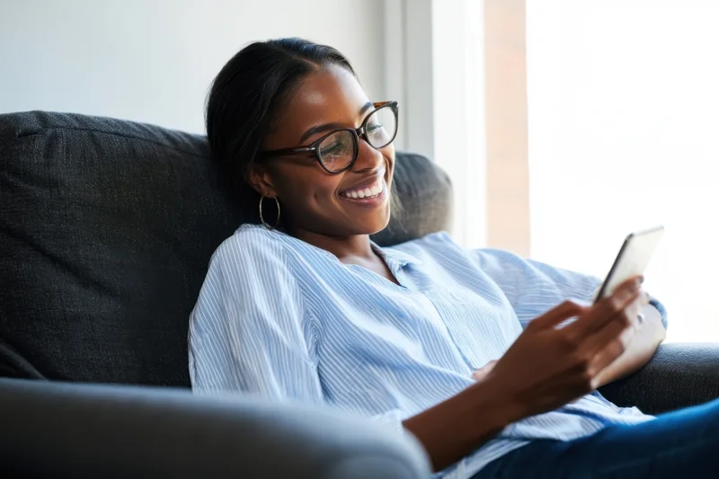 Young woman smiling while using smartphone on couch at home