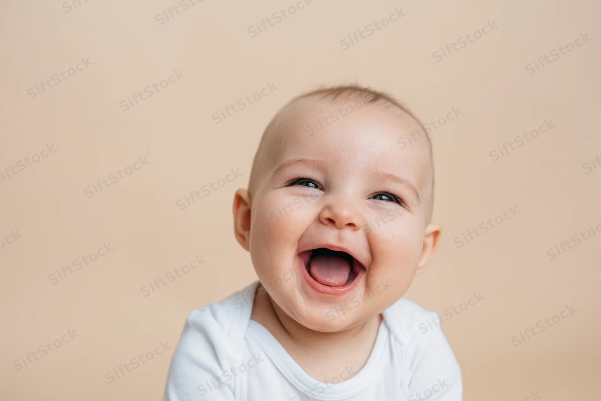 Baby laughing with wide open mouth and crinkled eyes in studio portrait