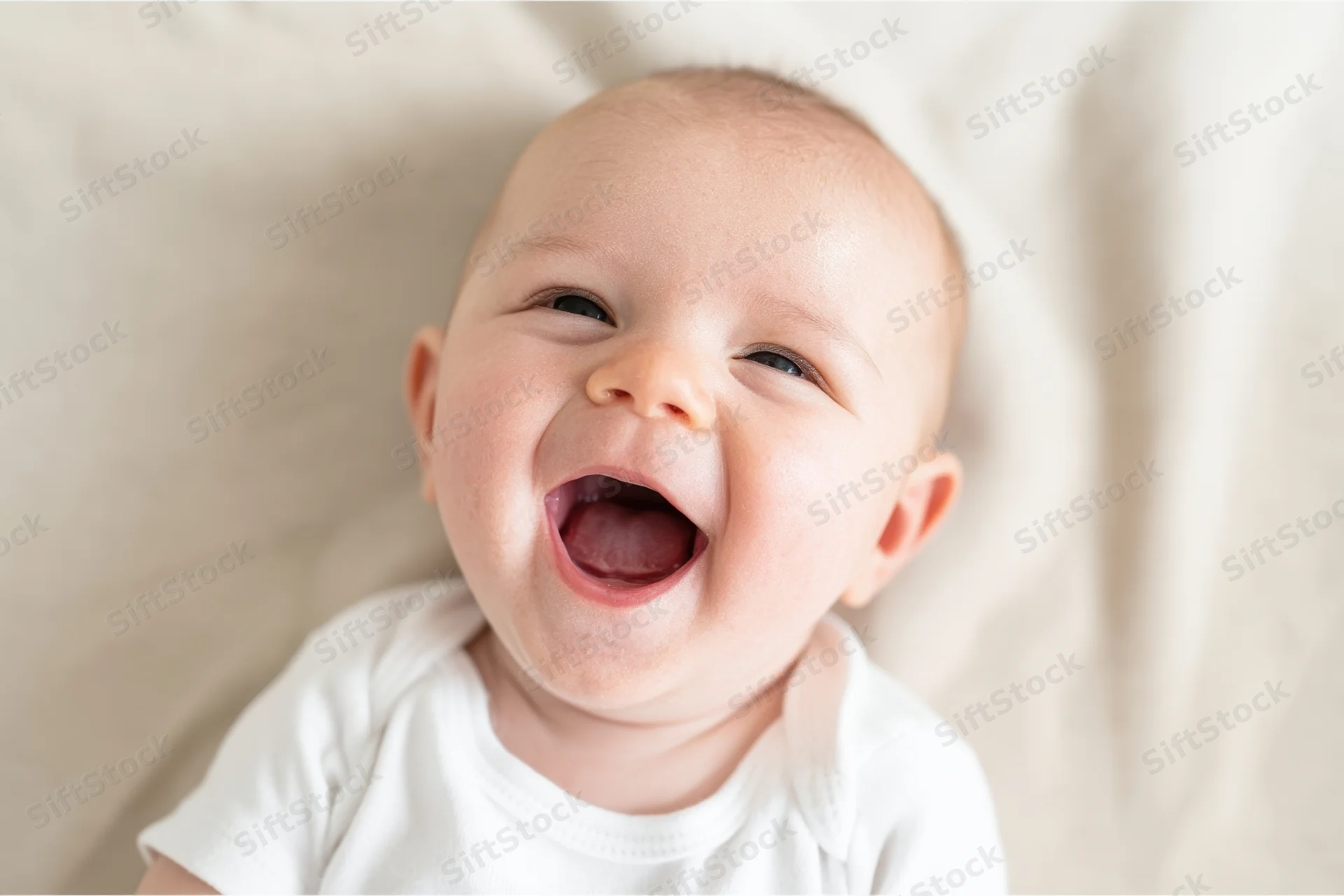 Baby laughing with wide open mouth and crinkled eyes on soft blanket