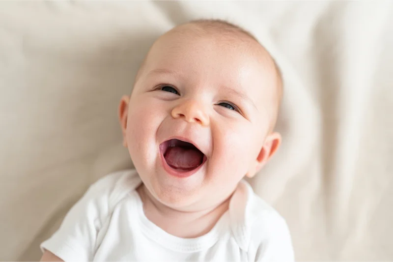 Baby laughing with wide open mouth and crinkled eyes on soft blanket