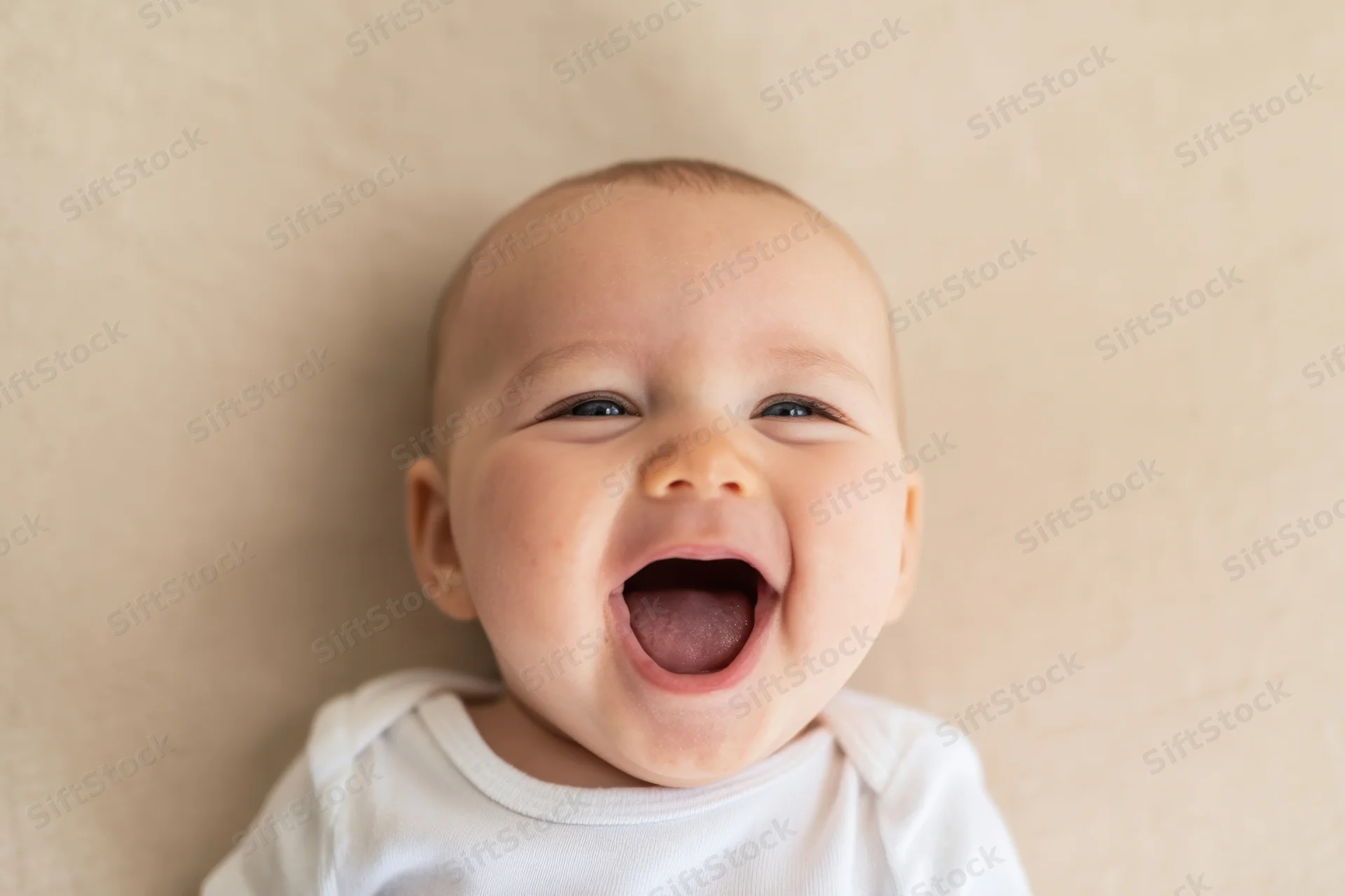 Baby laughing with wide open mouth and crinkled eyes on soft beige surface