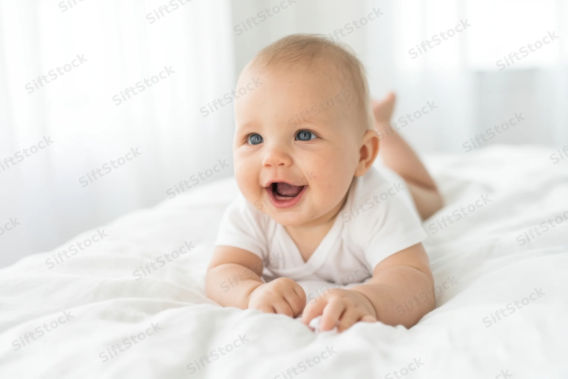 Smiling baby lying on white bed wearing white onesie