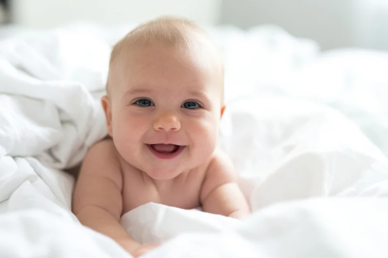Smiling baby lying on white bedding in soft natural light