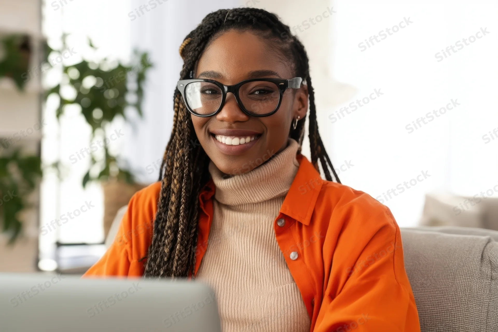 Smiling woman with braided hair and glasses sitting at laptop in home office