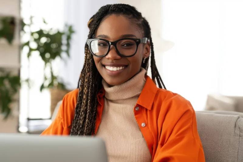 Smiling woman with braided hair and glasses sitting at laptop in home office