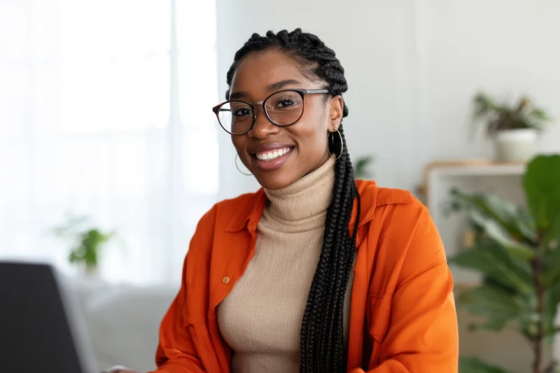 Smiling woman with braided hair and glasses sitting at laptop in home office