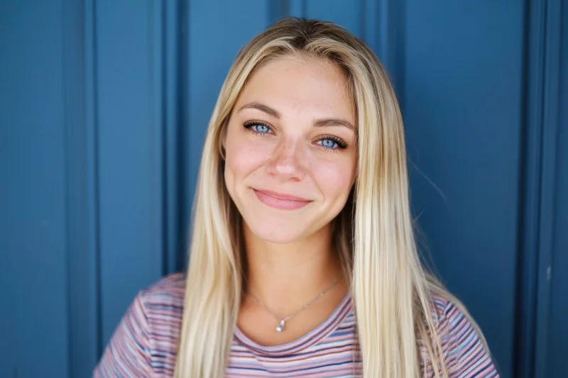 Young woman with long blonde hair and blue eyes smiling in front of blue panelled door