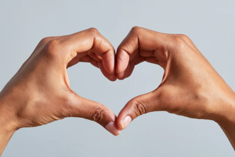 Two hands forming a heart shape against a plain light background