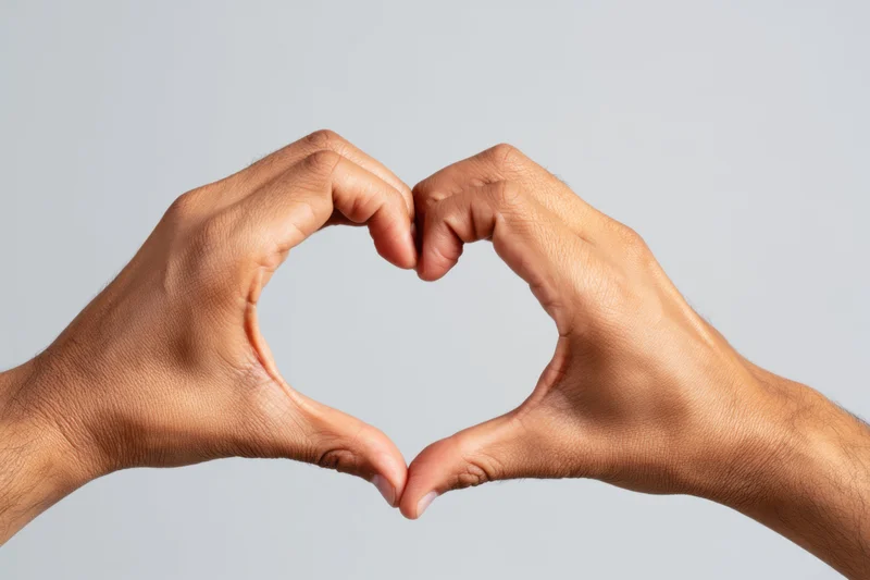Two hands forming a heart shape against a plain gray background