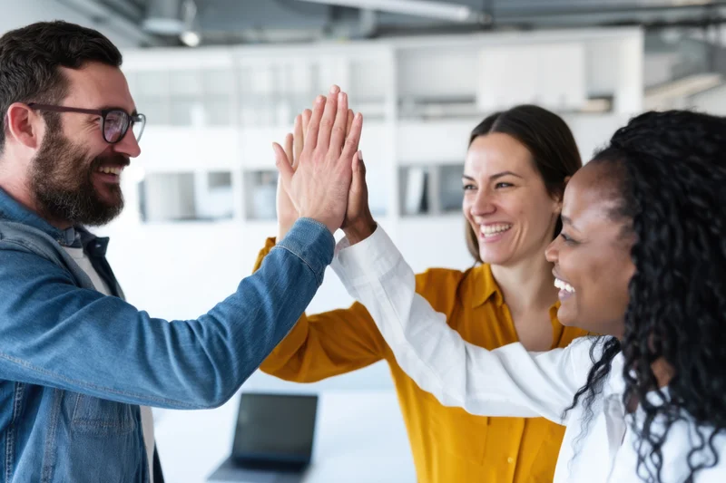 Three colleagues giving high five in modern office space