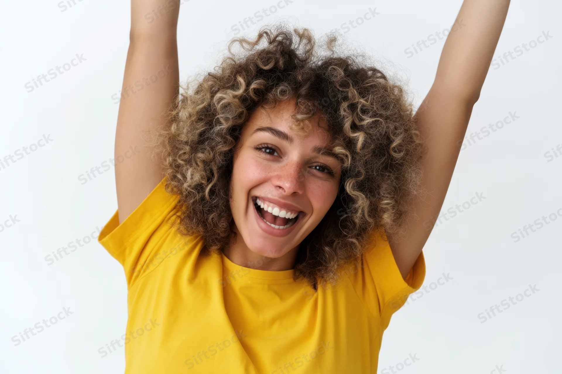 Cheerful woman with curly hair raising arms in joy, wearing yellow t-shirt against white background