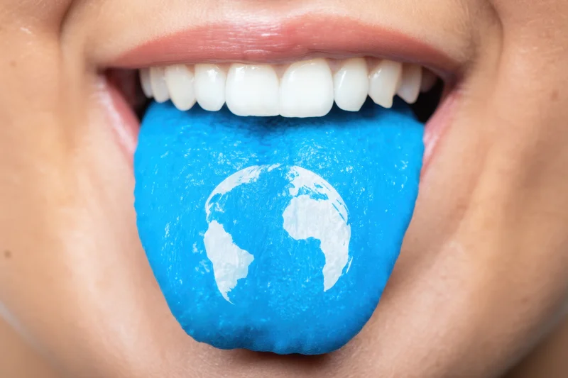 Close-up of a person's mouth with a blue tongue featuring a white globe map between the teeth