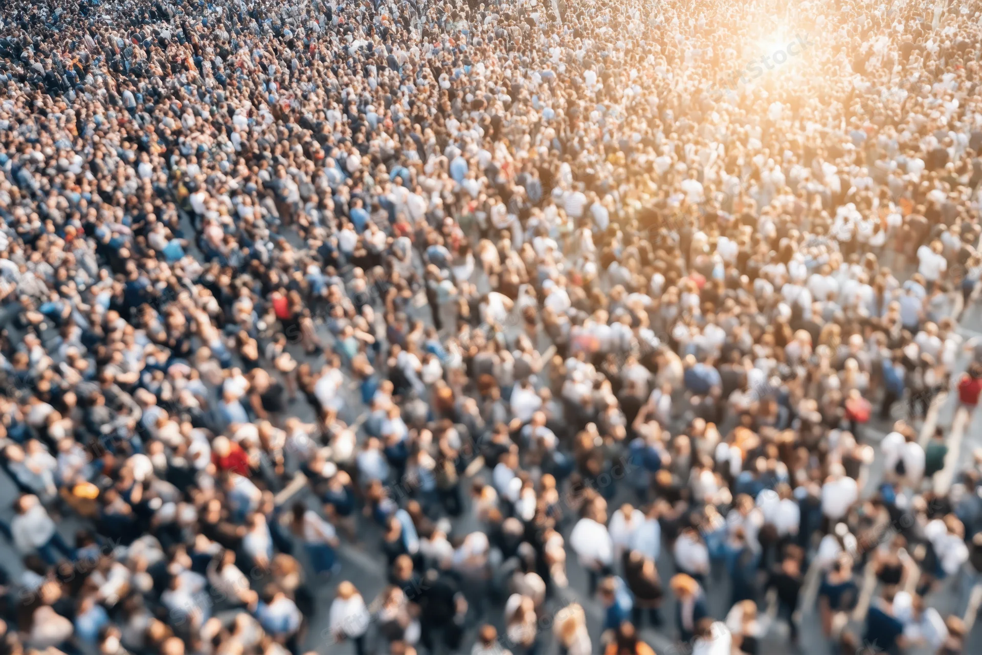 Aerial view of a dense crowd of people gathered in an urban street during daytime with sunlight creating a lens flare effect