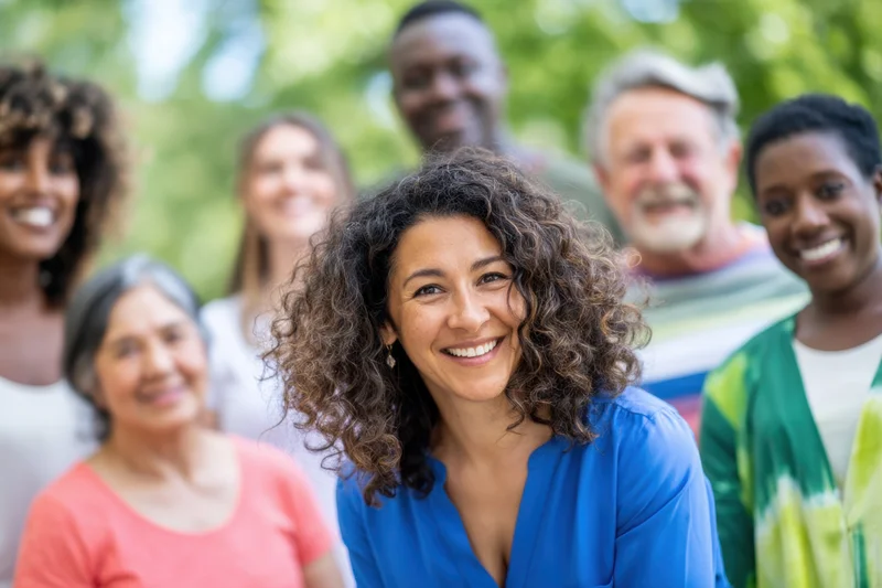 Woman smiling at camera with diverse group of people in a sunlit park