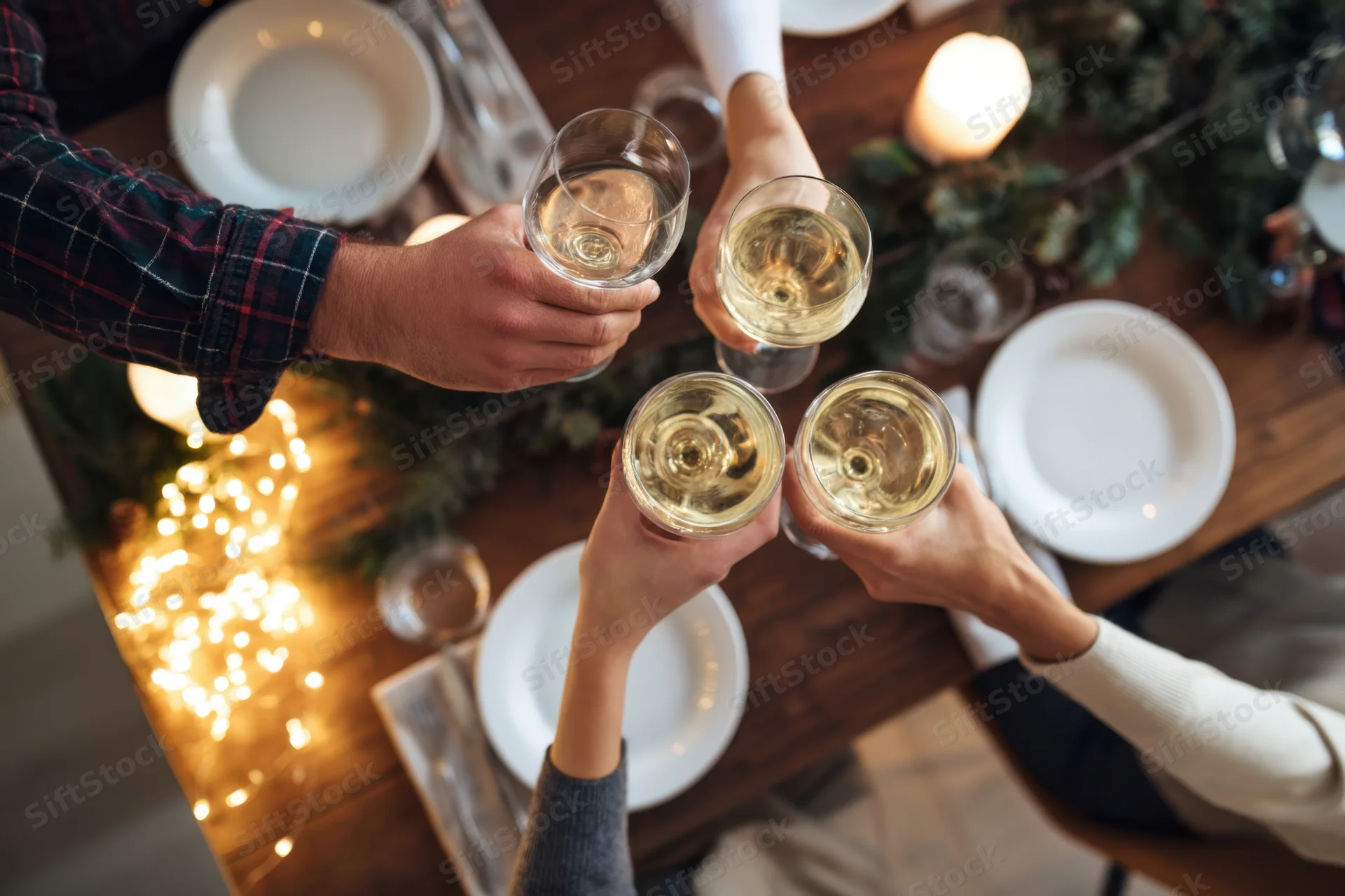 Four hands toasting with wine glasses over a decorated holiday dinner table