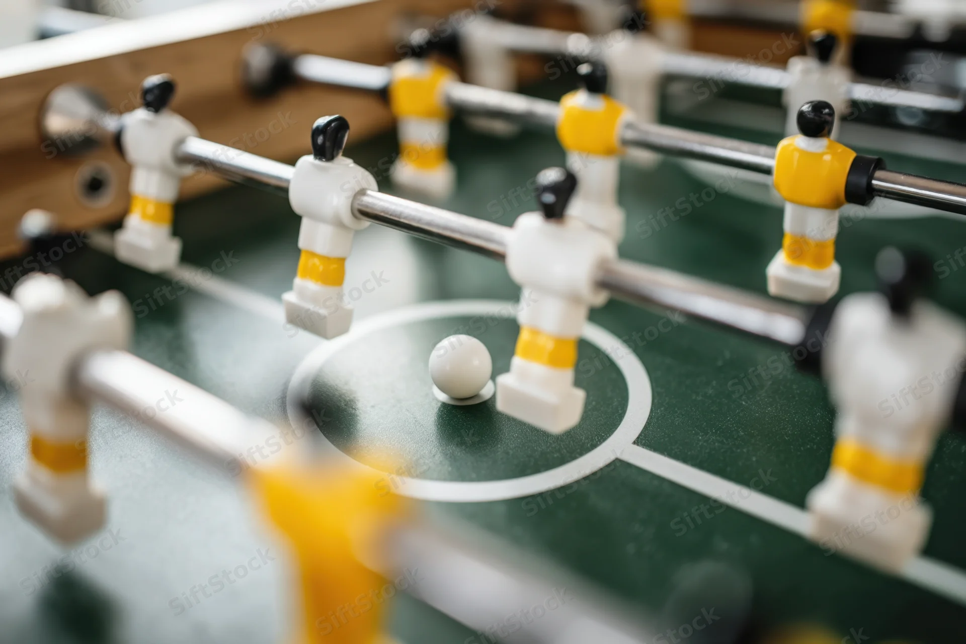 Closeup of foosball table with miniature players in white and yellow uniforms on green field