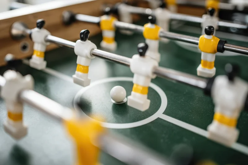 Closeup of foosball table with miniature players in white and yellow uniforms on green field