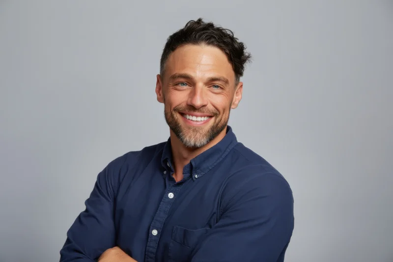 Smiling man in navy shirt with arms crossed against grey background