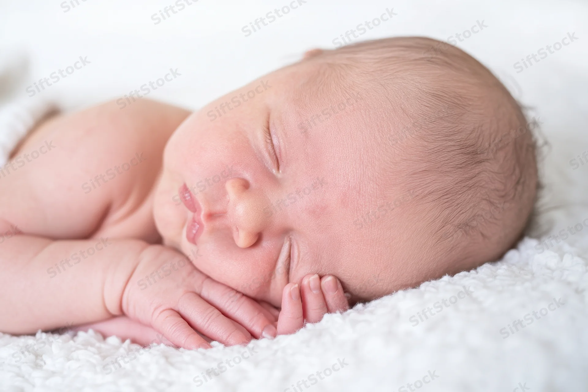 Newborn baby sleeping with hands folded near cheeks on white textured blanket
