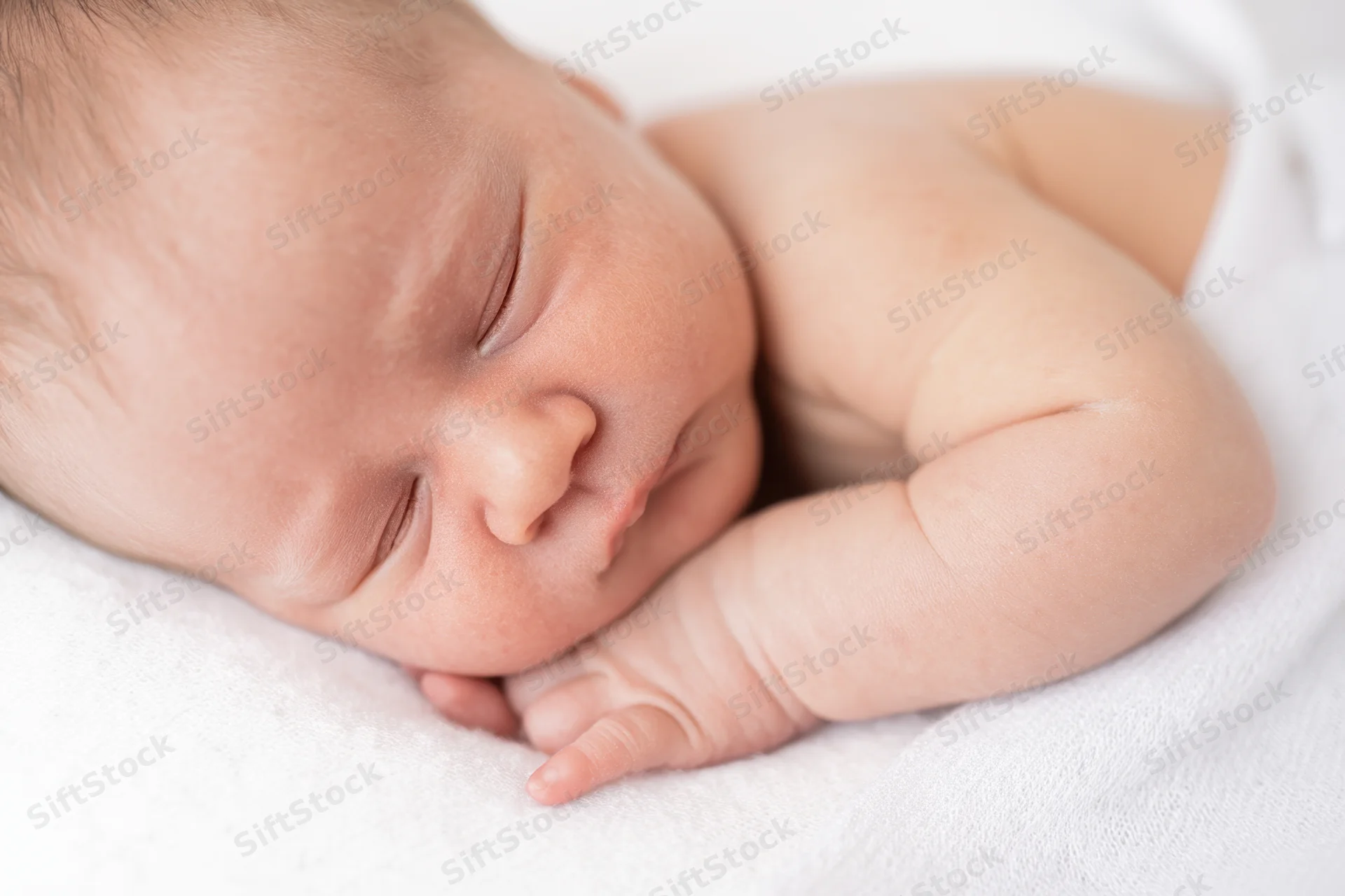 Newborn baby sleeping peacefully with tiny hands folded near the cheek on a white towel