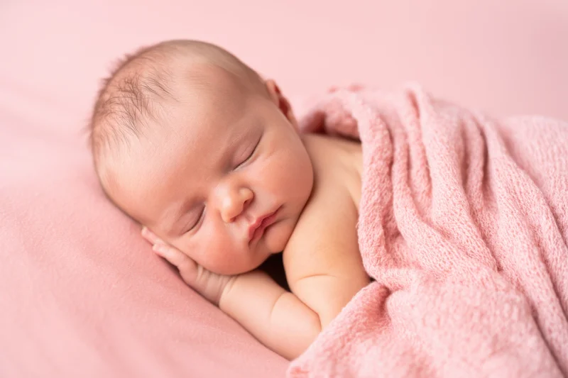 Newborn baby sleeping peacefully wrapped in a soft pink blanket on a pink surface