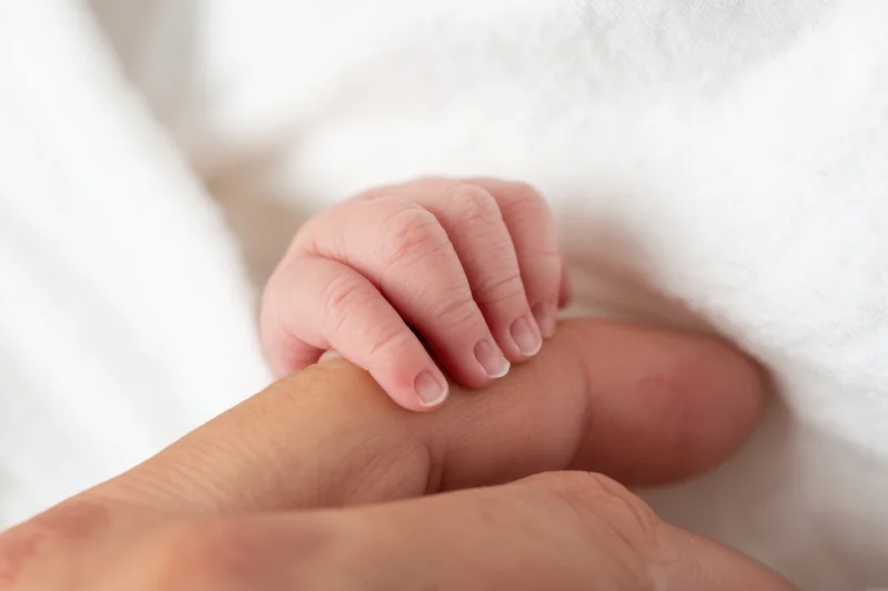 Newborn baby’s hand gently gripping an adult’s finger wrapped in white blanket