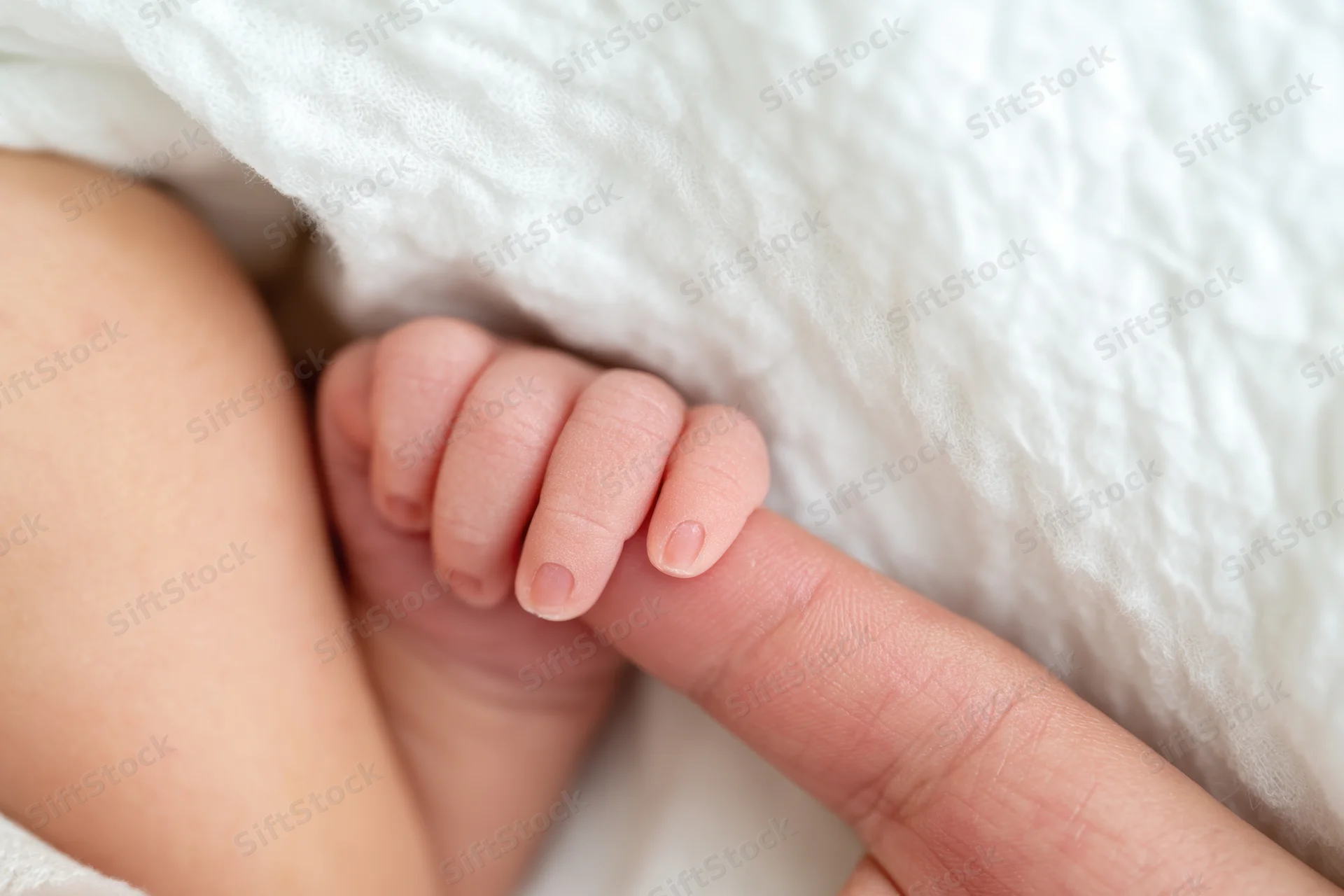 Newborn baby's tiny hand gripping an adult finger resting on a white blanket