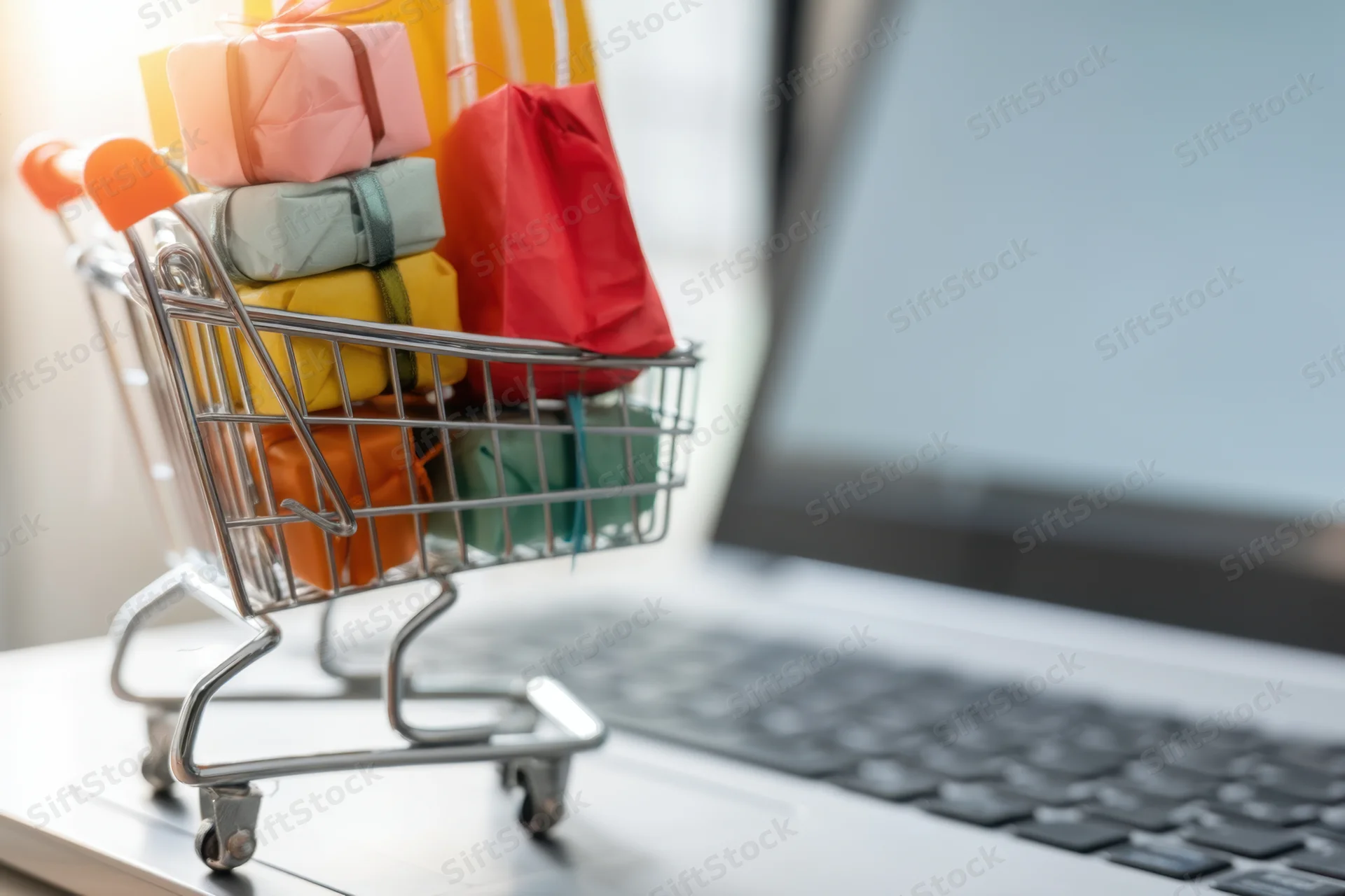 Miniature shopping cart filled with colorful gift boxes on a laptop keyboard