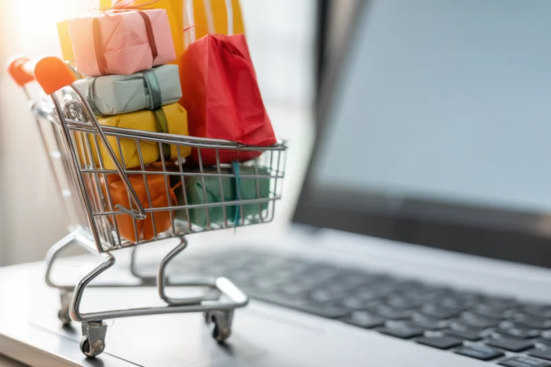 Miniature shopping cart filled with colorful gift boxes on a laptop keyboard