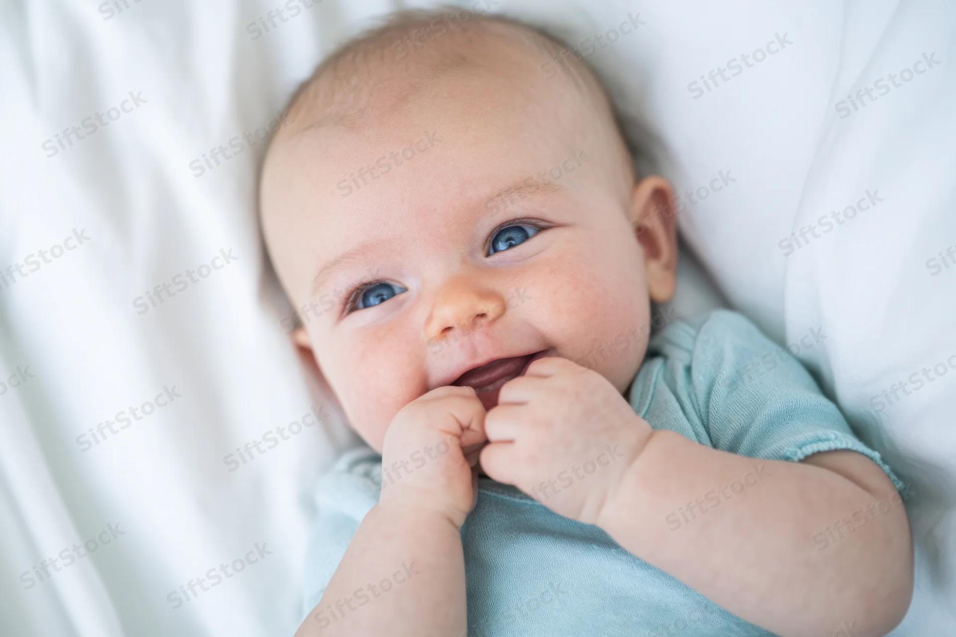 Smiling baby lying on white bed wearing light blue clothing